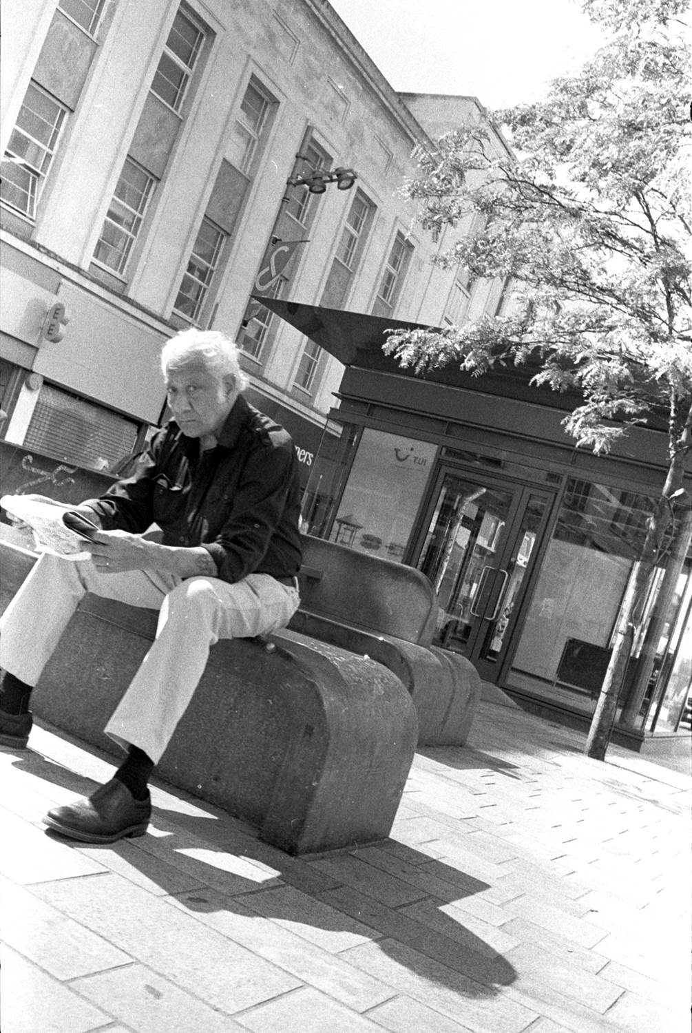 Vintage style old man sat on bench reading a newspaper 
