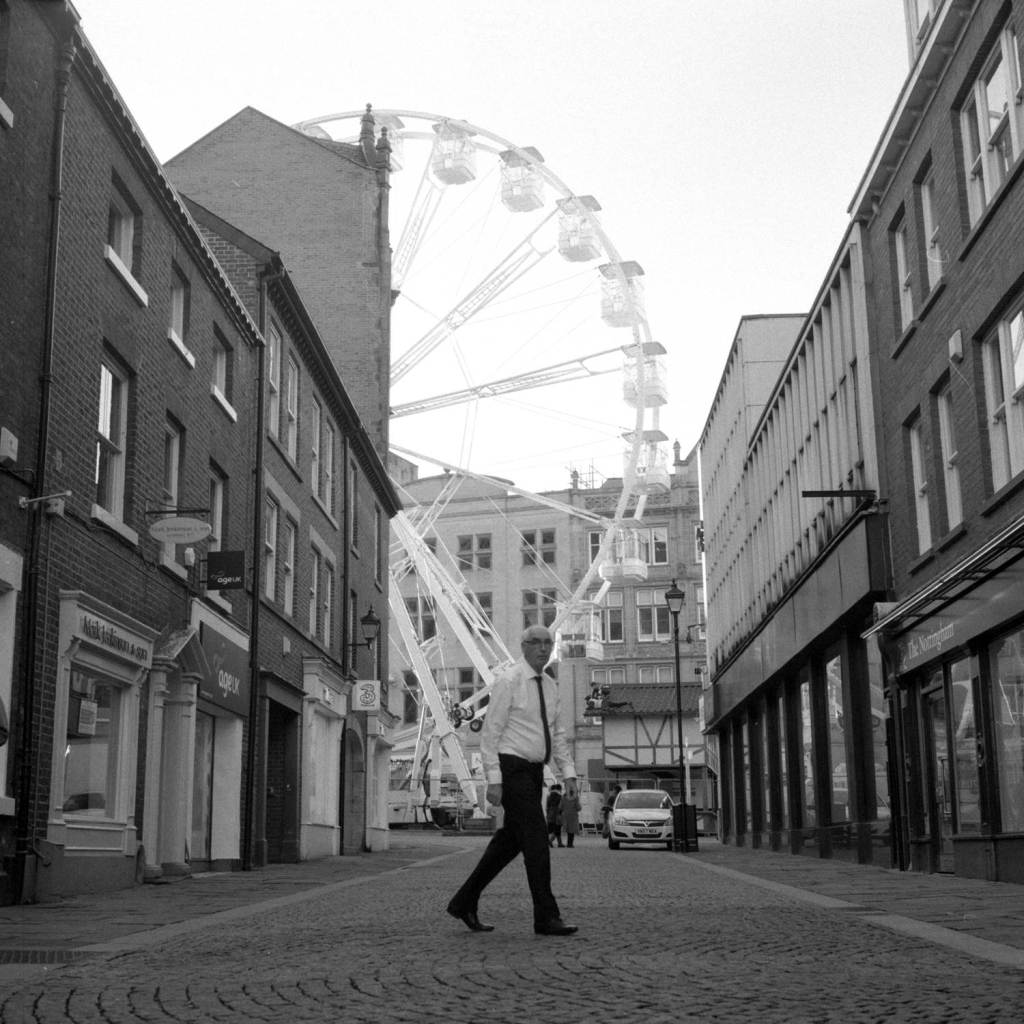 Smartly dressed Man walks through Sheffield City Centre with Ferris wheel in background